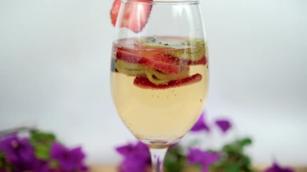 Minum dengan strawberry dan iris kiwi dalam gelas anggur dengan latar belakang putih — Stok Video