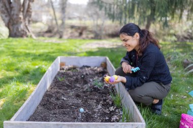Güzel esmer kadın boş bir saksı kutusunda paskalya yumurtası saklıyor.
