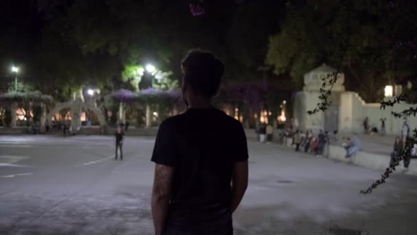 Молодой человек смотрит на людей в парке ночью — стоковое видео