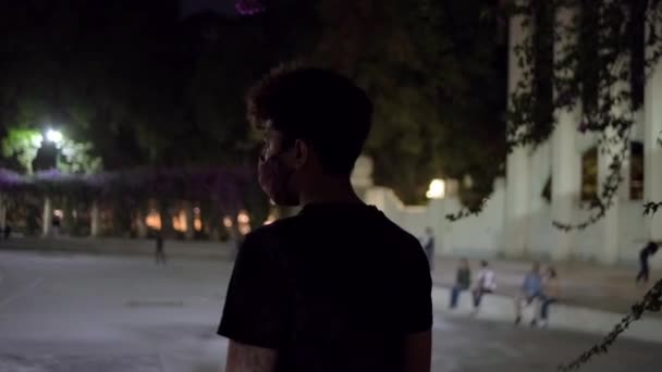 Молодой человек смотрит на людей в парке ночью — стоковое видео