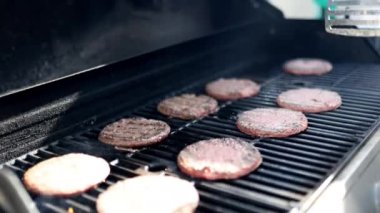 Demir ızgarada çiğ hamburger çeviren erkek el.