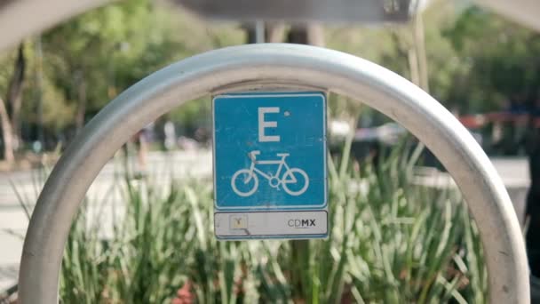 Blue bicycle parking spot sign on metal arch with trees as background — Stock Video