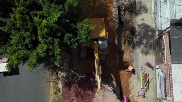 Vista aérea de una excavadora excavando en el sitio de construcción bajo un árbol — Vídeos de Stock