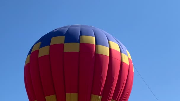 Aquecimento e inflar um balão de ar quente colorido sob o céu azul — Vídeo de Stock
