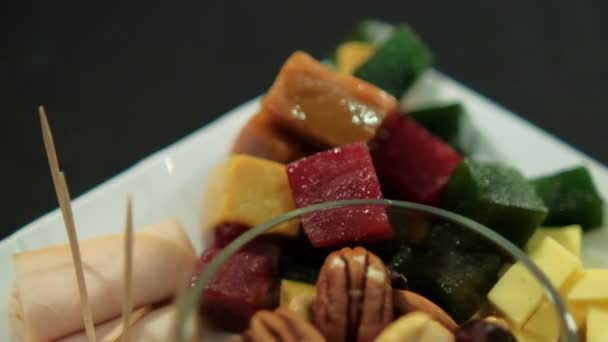 Šunkové závitky, nakrájená ovocná pasta, kostky sýra a ořechy na bílém talíři — Stock video