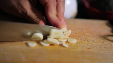 Tahta kesme tahtasına sarımsaklı karanfil kesen eller.