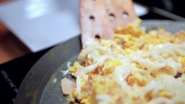 Spatula çırpılmış yumurta, doğranmış jambon ve erimiş Oaxaca peyniri topluyor.
