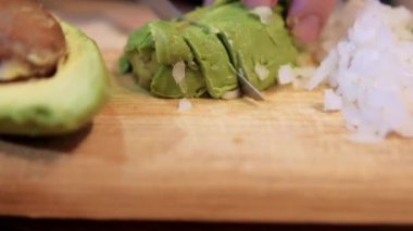 Avokado ve soğanı kesme tahtasında dilimleyen eller.