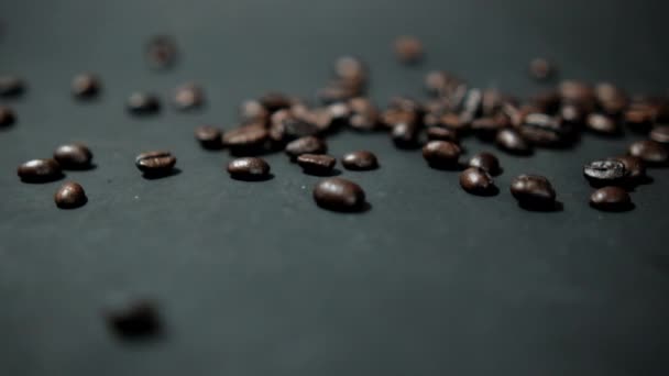 Bando de grãos de café torrados sendo derramados sobre a superfície preta — Vídeo de Stock