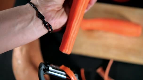 Manos pelando zanahoria fina con pelador de juliana por encima de la tabla de cortar — Vídeo de stock