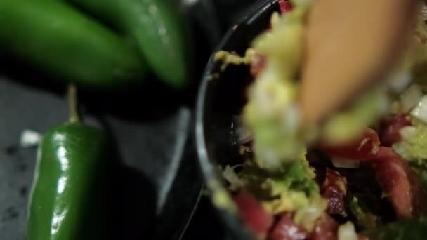 Wooden spoon preparing guacamole next to three chili peppers — Stock Video