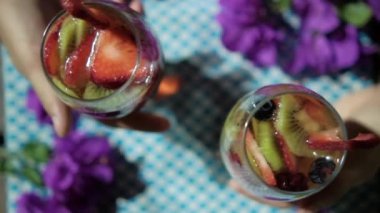 Kareli peçetenin üzerinde meyve dilimleri olan içkileri tutan iki elin üst görüntüsü