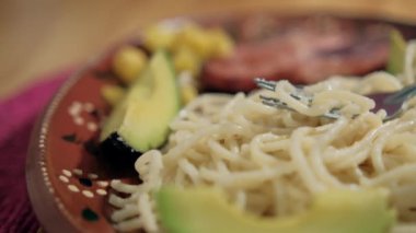 Geleneksel kil tabağın üzerinde beyaz spagetti ve avokado dilimleri var.