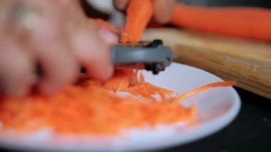 Eller ince havuç soyarken jülyen soyacağı beyaz tabağın üstünde.