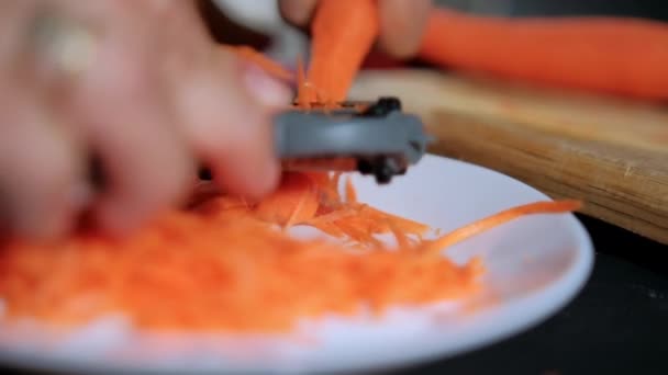 Hands peeling thin carrot with julienne peeler above white plate — Stock Video