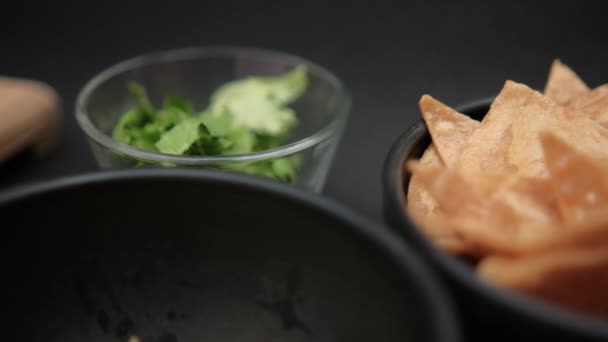 Tigelas de abacate picado, lascas de tortilla e alface na superfície preta — Vídeo de Stock