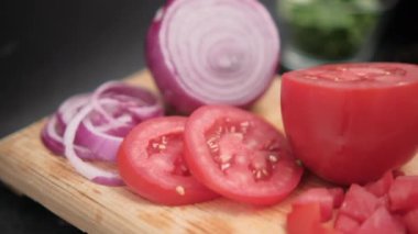 Dilimlenmiş domates ve soğan ahşap kesim tahtasında bulanık arka planda.