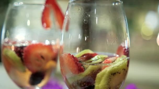 Dos bebidas con rebanadas de fruta en copas de vino con fondo borroso — Vídeos de Stock