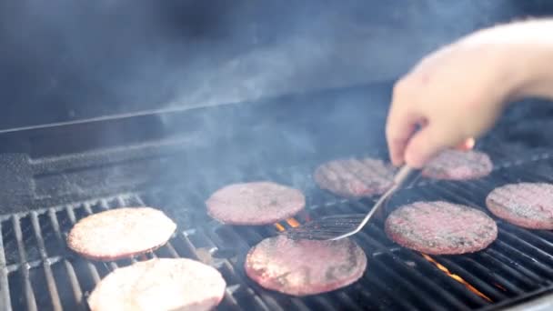 Мужская рука перелистывает сырое мясо гамбургера на железный гриль барбекю — стоковое видео