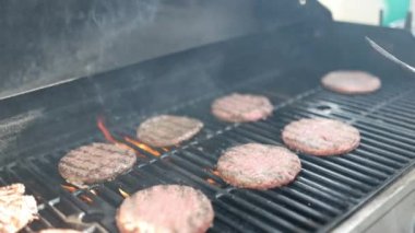 Demir ızgarada çiğ hamburger çeviren erkek el.