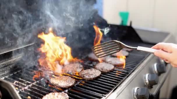 Чоловік перевертає м'ясо гамбургерів над вогнем гриля для барбекю — стокове відео