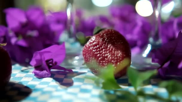 Ποτήρι κρασιού, μοβ λουλούδια, και δύο φράουλες σε καρό τραπεζομάντιλο — Αρχείο Βίντεο