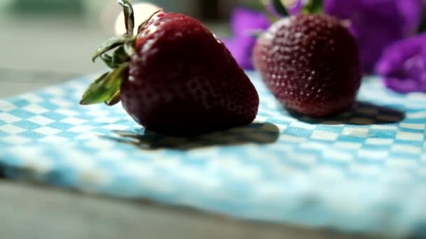Ein Paar Erdbeeren und lila Blumen auf einer karierten Tischdecke — Stockvideo