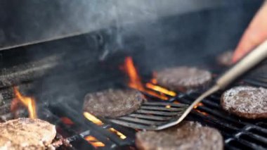 Erkek el mangal ızgarasının yüksek alevi üzerinde hamburger eti çeviriyor.