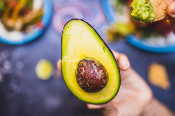 Hand holding an avocado half above blurry background — Stock Photo, Image