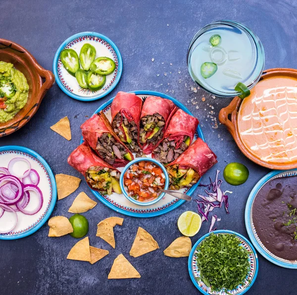 Pyszne burrito i więcej meksykańskich przypraw i dań na ciemnej powierzchni — Zdjęcie stockowe