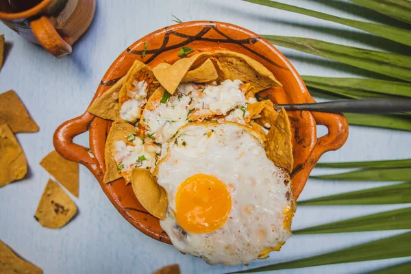 Lergryta med chilaquiles med stekt ägg ovanpå och ovanför vit yta — Stockfoto