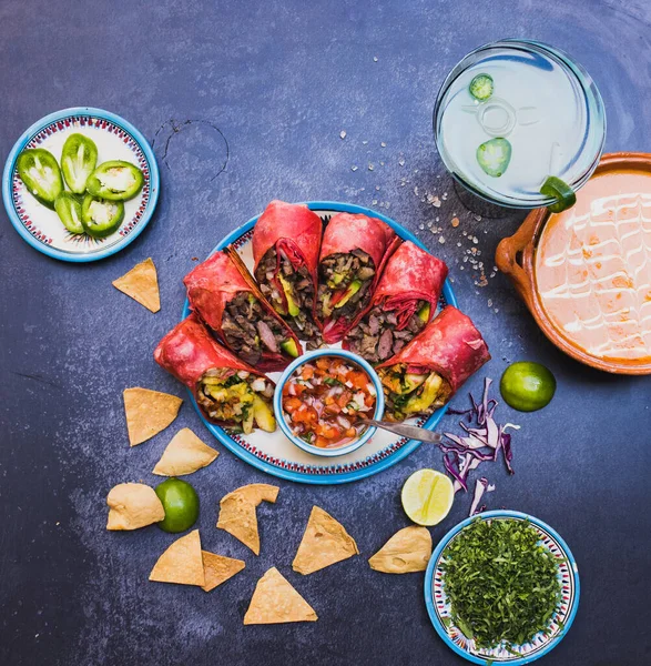 Pyszne burrito i meksykańskie przyprawy na ciemnej powierzchni — Zdjęcie stockowe
