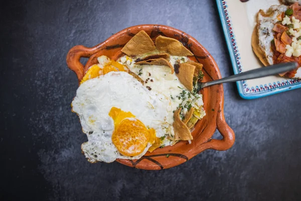 Huevo frito y chips de tortilla en maceta de arcilla tradicional sobre la superficie oscura — Foto de Stock