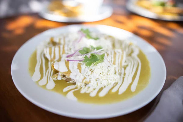 Talíř lahodných zelených mexických enchilád na hnědém stole — Stock fotografie