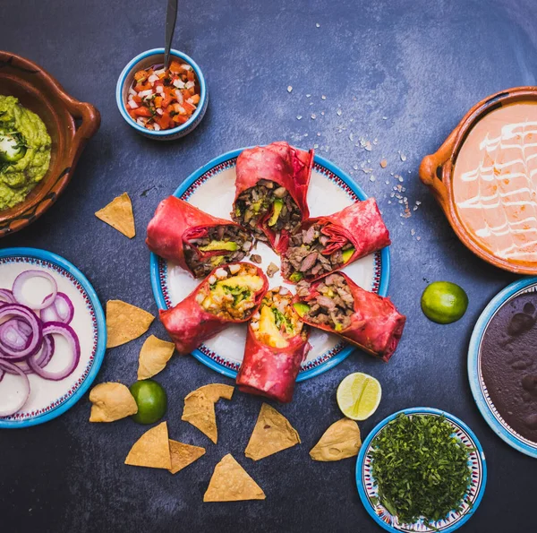 Deliciosos burritos e mais condimentos mexicanos e pratos na superfície escura Imagem De Stock