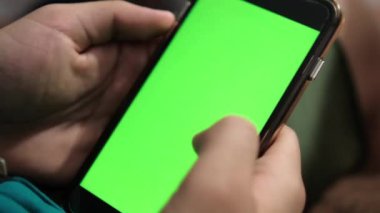 Parlak yeşil ekranlı siyah bir akıllı telefon tutan eller.