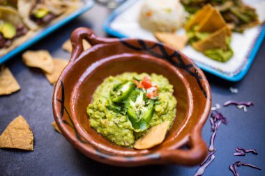 Lezzetli baharatlı guacamole. Koyu yüzeyin üstünde geleneksel kil çömlek.