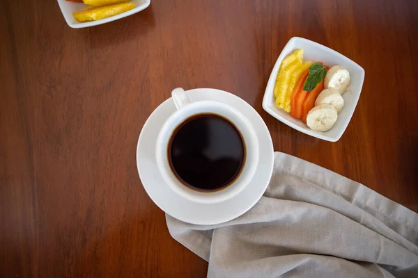 Kopje koffie en klein bord met verse fruitschijfjes op bruine tafel — Stockfoto