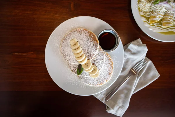 Panquecas saborosas com açúcar em pó e banana fatiada na mesa marrom Fotografia De Stock