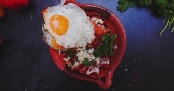 Skål med chilaquiles med stekt ägg ovanpå och ovanför mörk yta — Stockvideo