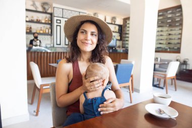 Güzel gülümseyen anne restoranda kucağında sevimli bir bebek tutuyor.