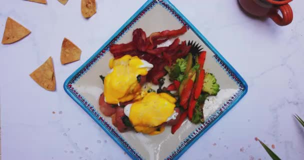 Placa de deliciosos huevos benedicto y verduras asadas en la superficie blanca — Vídeos de Stock