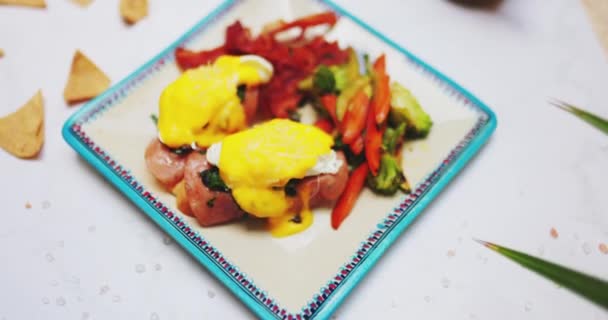 Placa de deliciosos huevos benedicto y verduras asadas en la superficie blanca — Vídeo de stock
