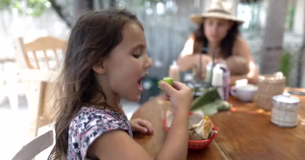 Schattig klein meisje aan houten tafel likken limoen met wazige achtergrond — Stockvideo