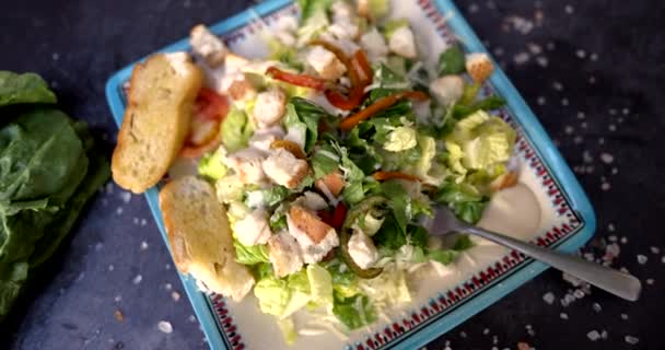 Placa de deliciosa ensalada rodeada de verduras y sal en la superficie negra — Vídeo de stock