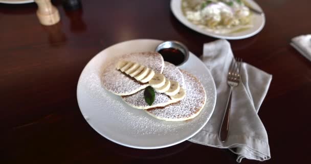 Smakrika pannkakor med florsocker och skivad banan ovanför brunt bord — Stockvideo