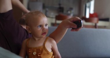 Küçük çocuk gri koltukta otururken kumandayı babasından almaya çalışıyor.