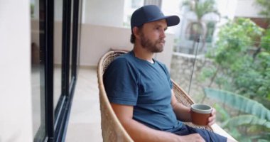 Mavi elbiseli bir adam arka planda bulanık yapraklı kahve içiyor.
