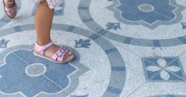 Mavi döşeme üzerinde yürüyen sevimli sandaletlerle çocuk ayakları.