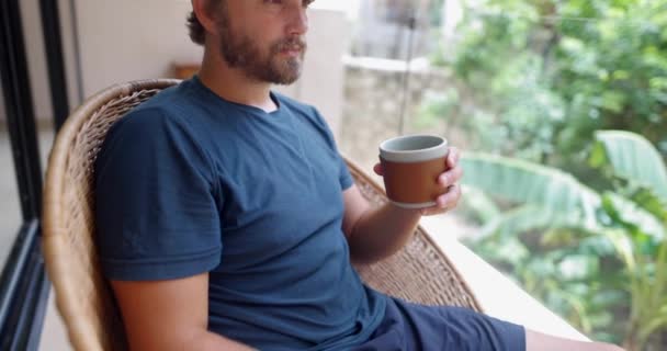 Человек в синей одежде пьет кофе с расплывчатыми листьями в качестве фона — стоковое видео